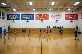 Show several  2ftx7ft horizontal vinyl banner inside school gym with team support and PDQ Signs logo advertisement